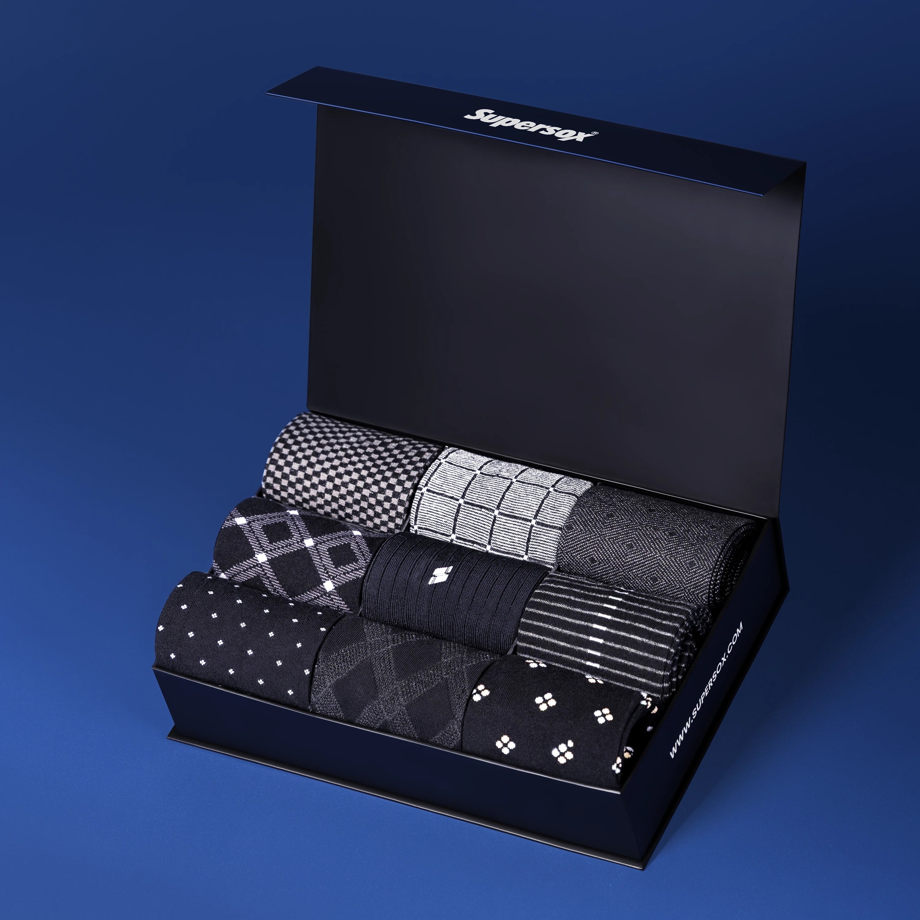 Supersox premium gift box containing six pairs of men’s dress socks in black and grey tones with subtle patterns.