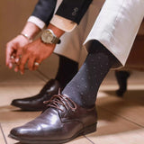 An image of a man wearing grey patterned formal socks with brown leather dress shoes and dark trousers.