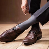 An image of a man adjusting grey dotted formal socks while wearing brown leather loafers and navy trousers.